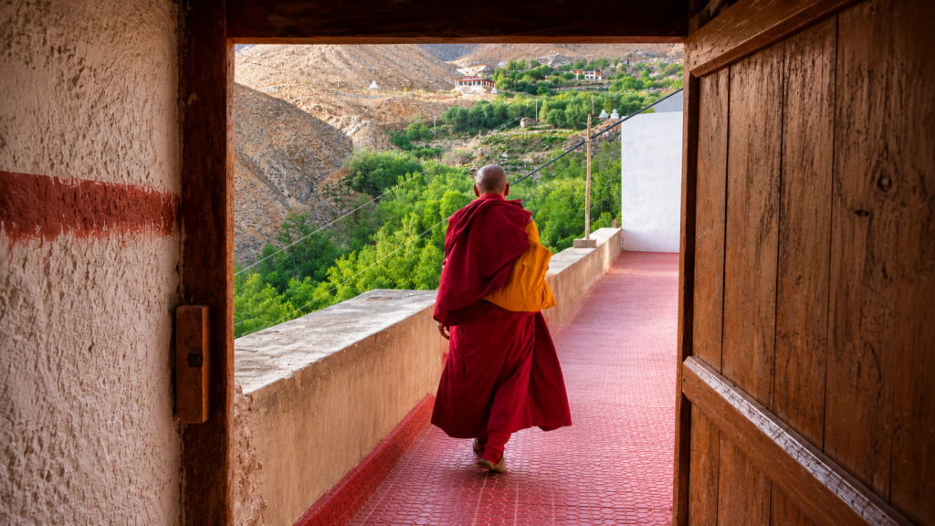 A Buddhist monk walking through a monastery doorway in Ladakh, symbolizing the journey of inner transformation.